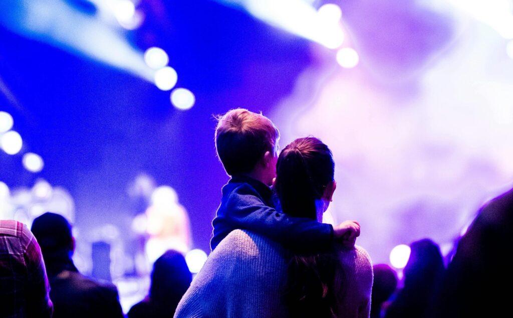 Woman holding child watching concert in arena - Caleb Oquendo